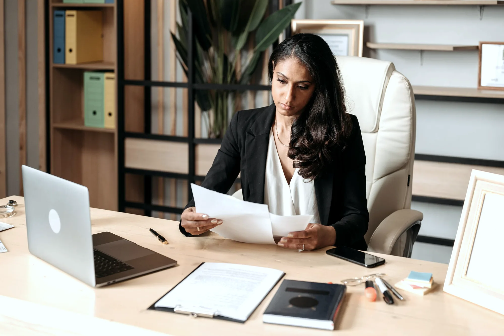 An accountant reading a printed page beside an open laptop at her desk.
