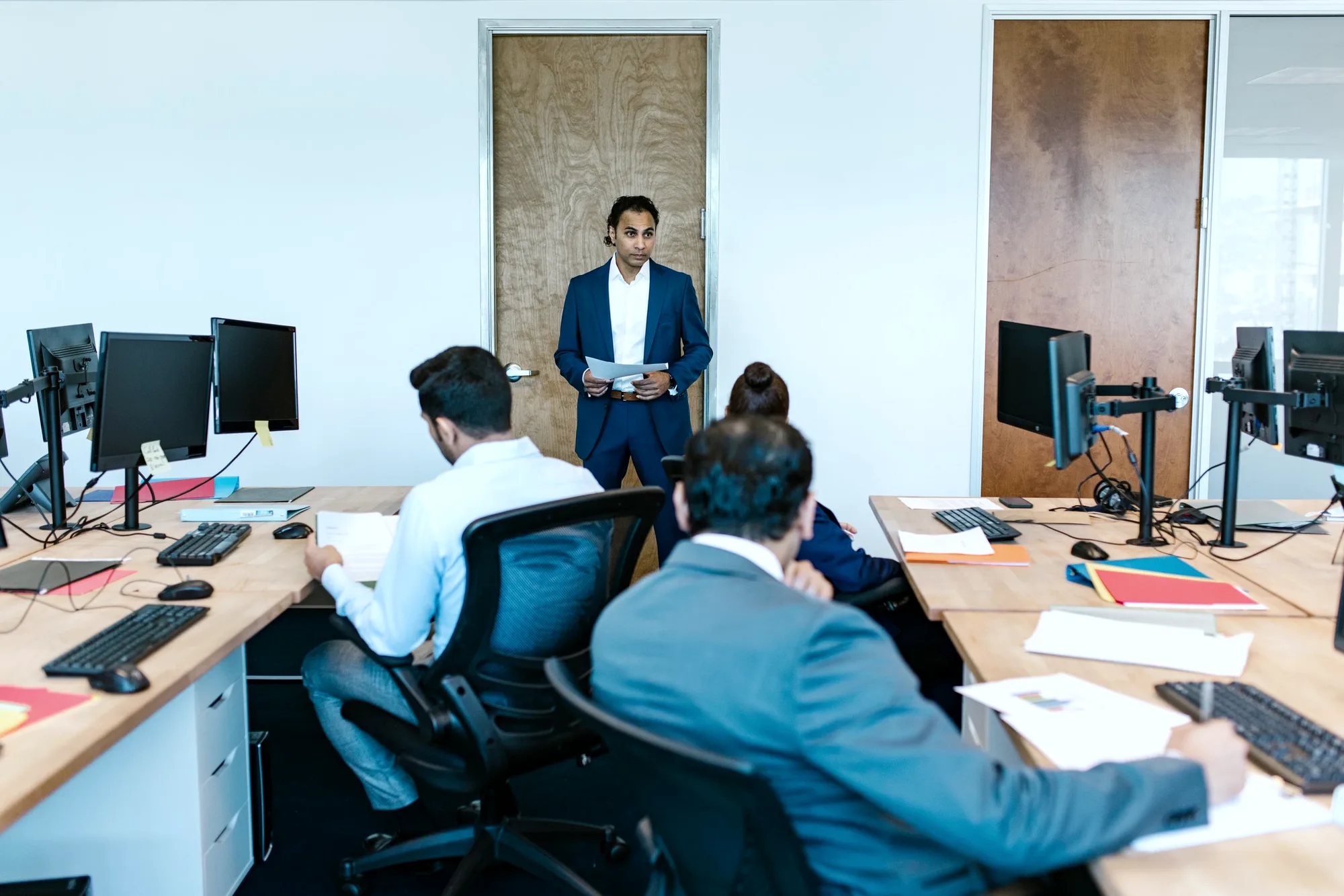 A finance colleague standing to speak with two seated teammates at their desks.