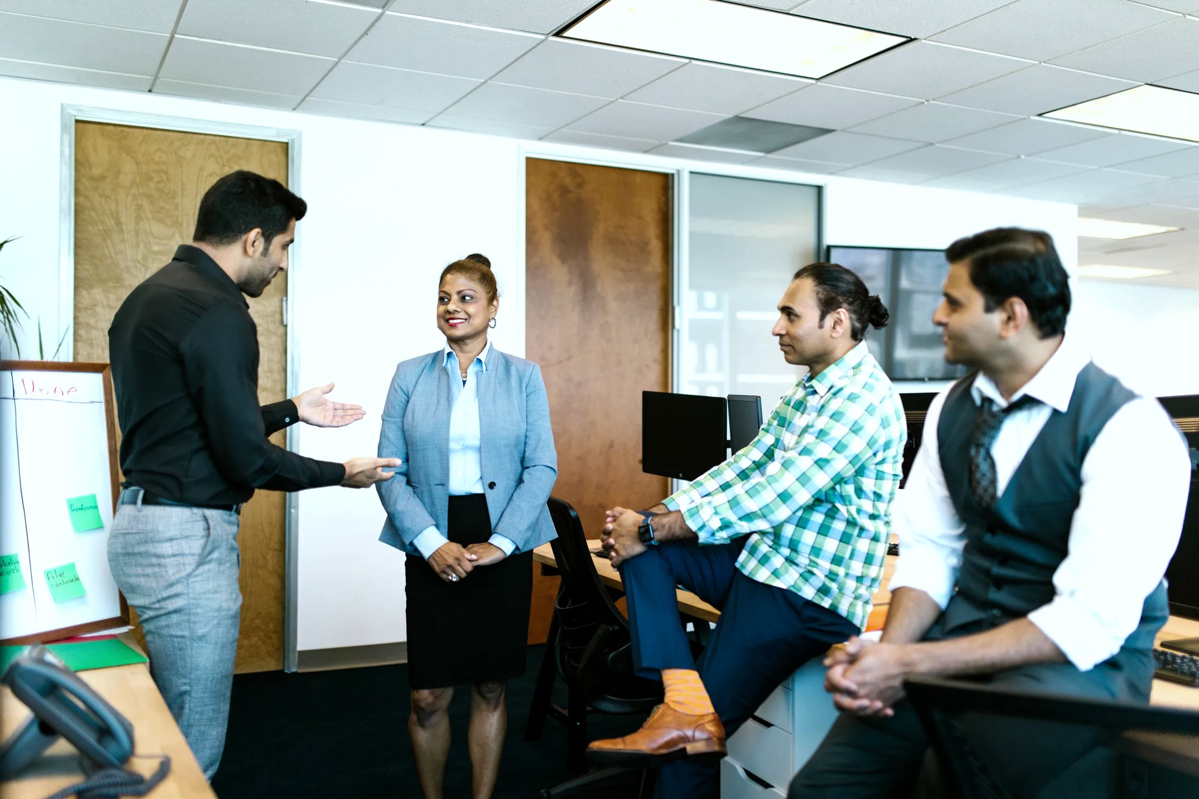 Four colleagues in conversation around a standing desk in an open-plan office.