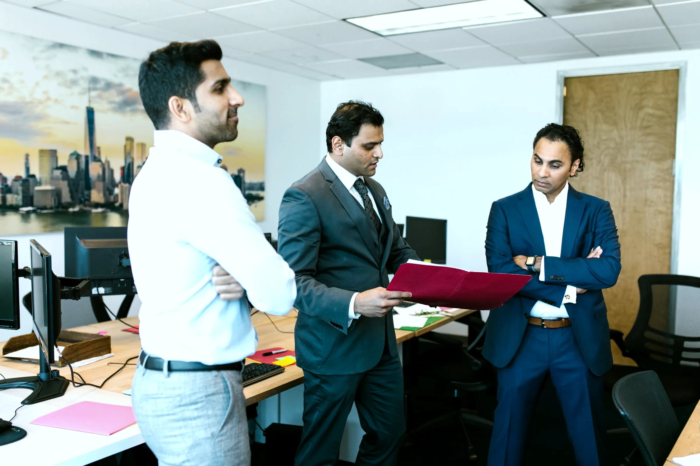 Three colleagues exchanging a printed page in a bright, open-plan office.