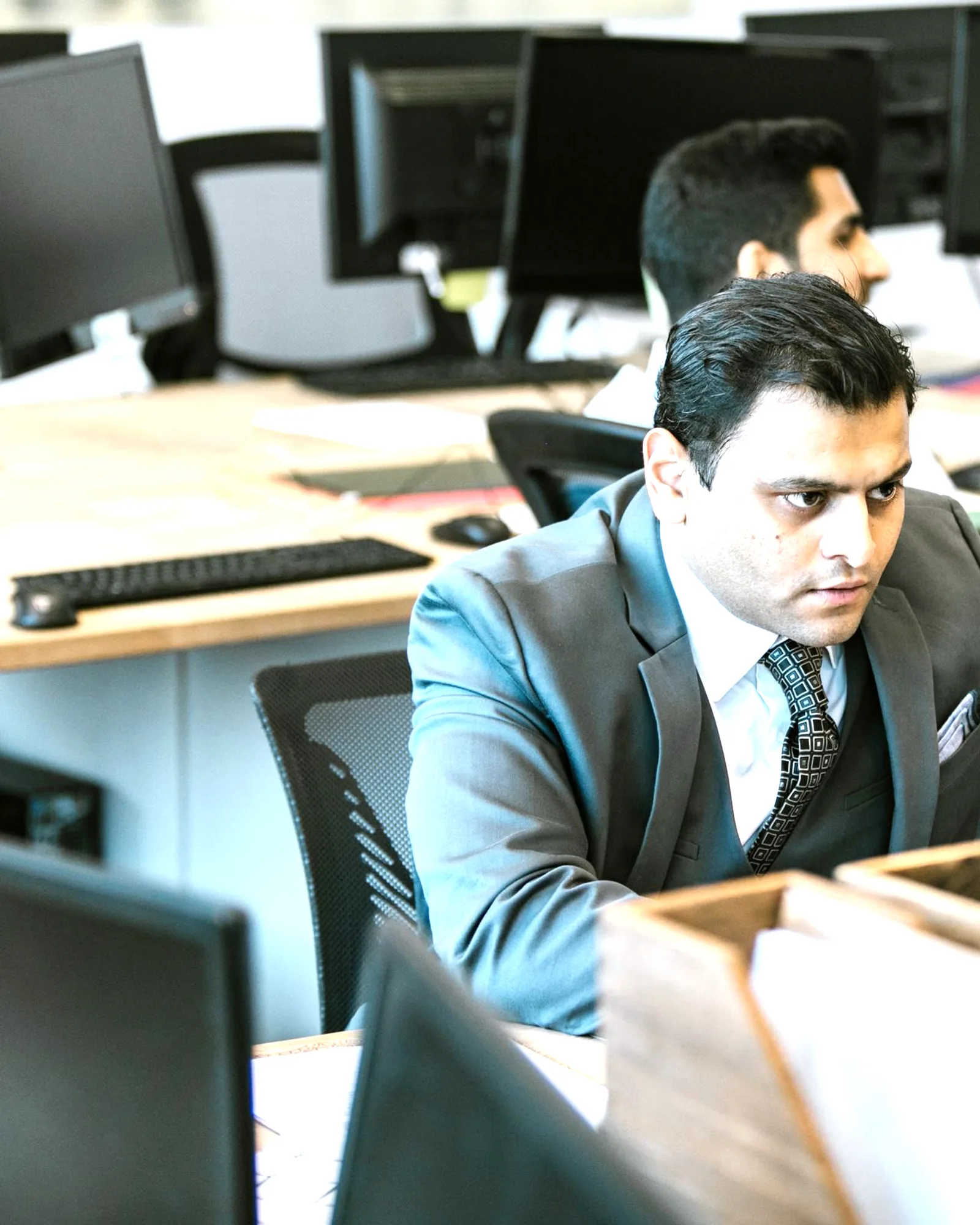 A colleague at his desk among busy monitors, focused on his own screen.