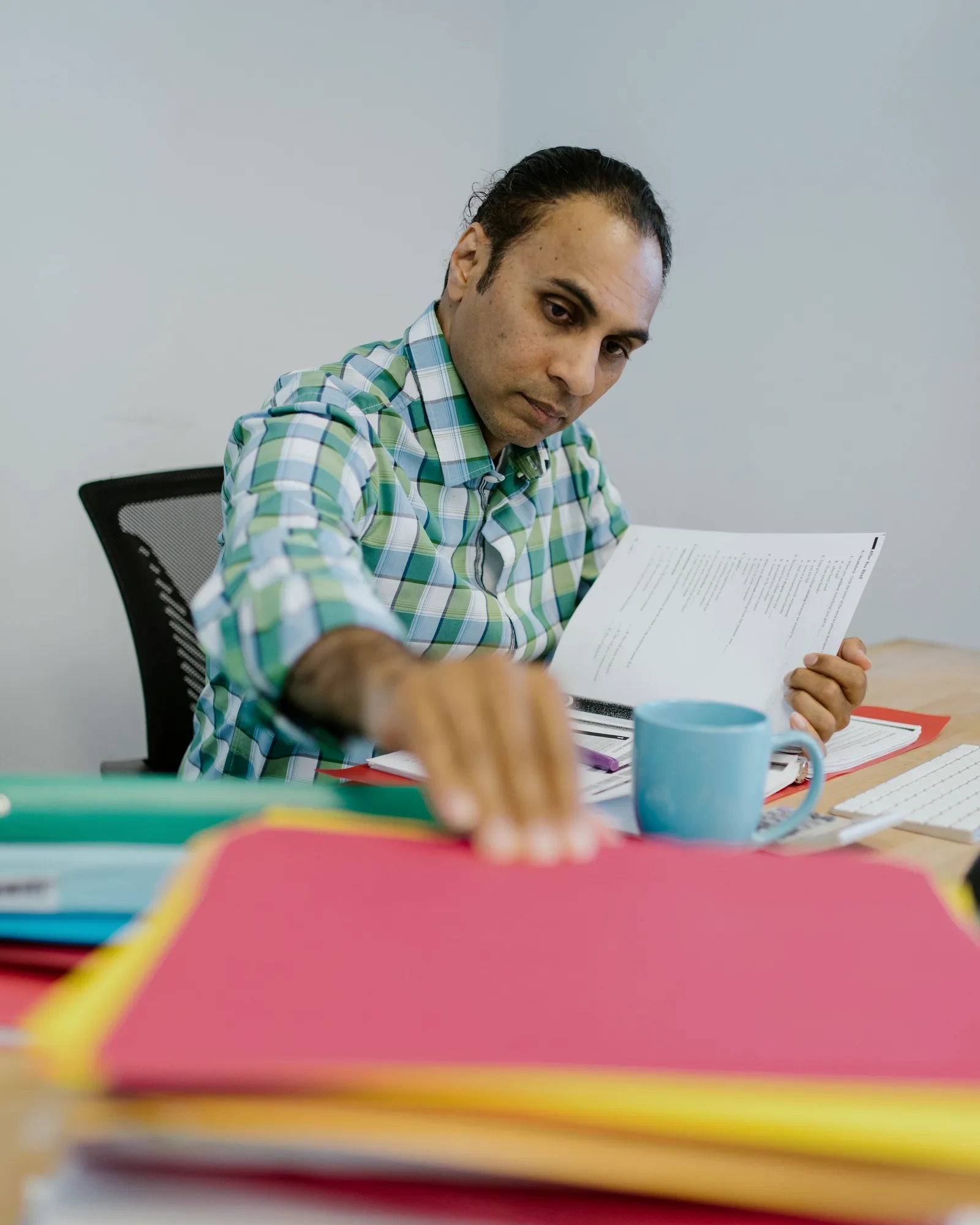 An auditor checking a printed page at his desk, pen in hand.