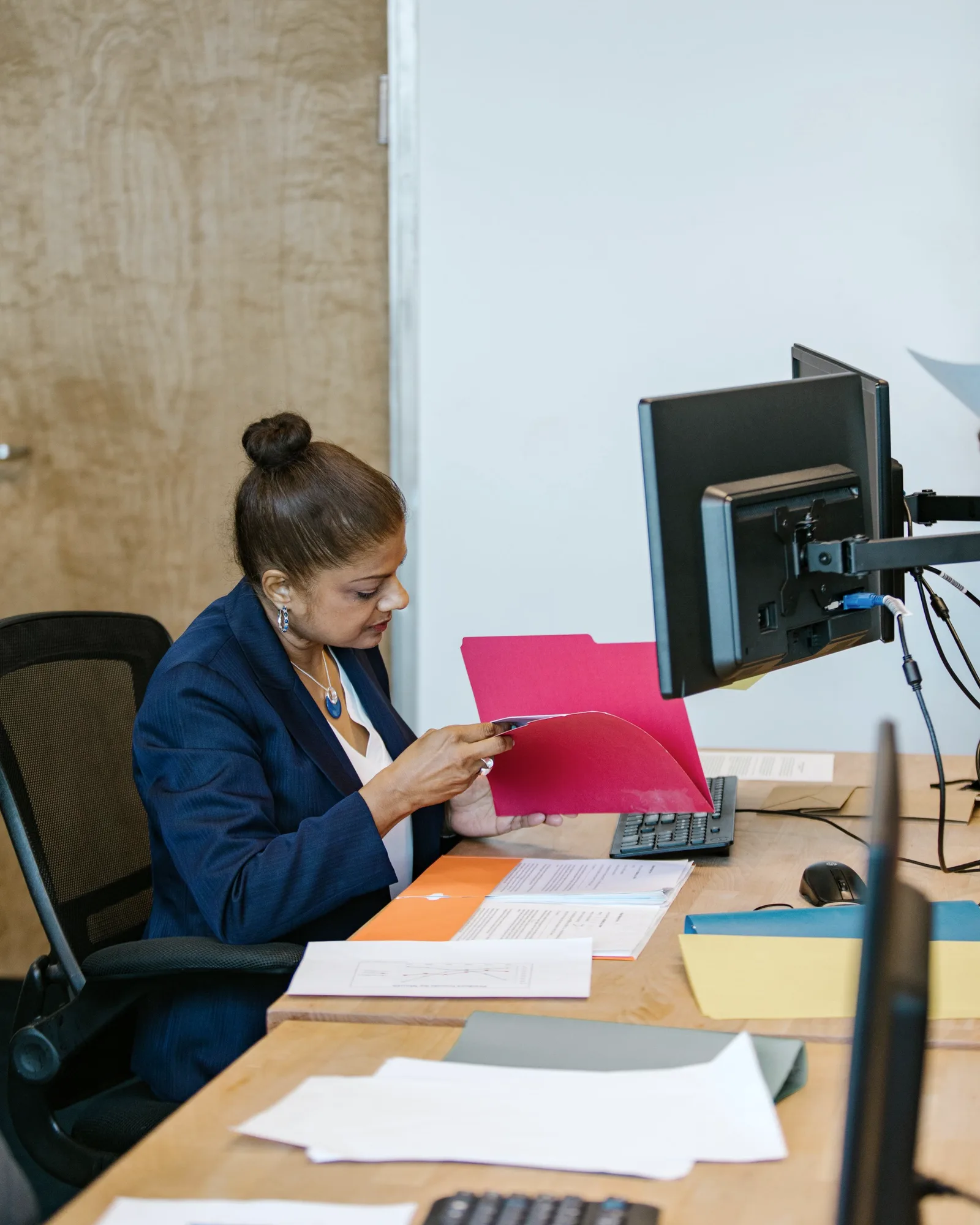 An accountant opening a folder at her desk, statements and a stack of folders in reach.