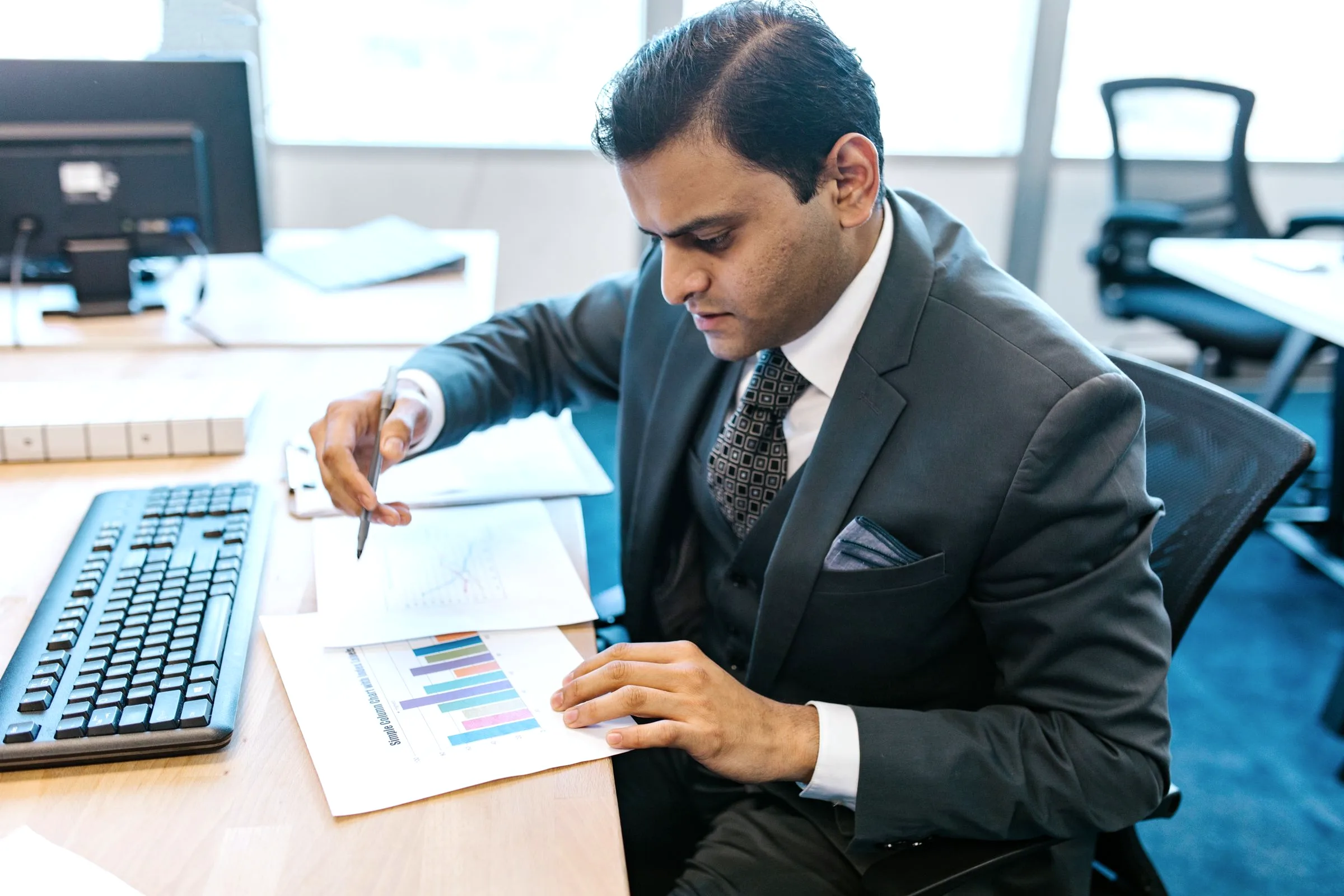 A finance professional pointing his pen at chart data on his desk.