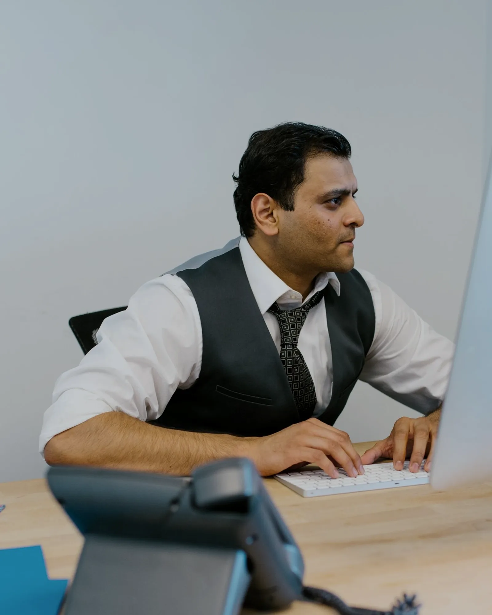 A finance professional at his iMac, focused, keyboard in hand.